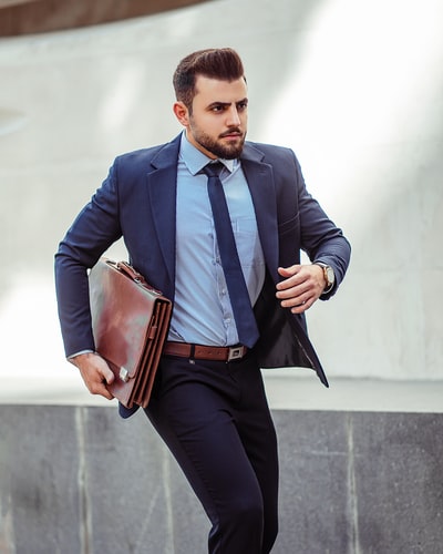 Dressed in a blue suit jacket and black trousers, carrying a brown bag
